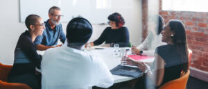 a group of 6 people sitting around a round table. They are smiling and look to be in the middle of a conversation.